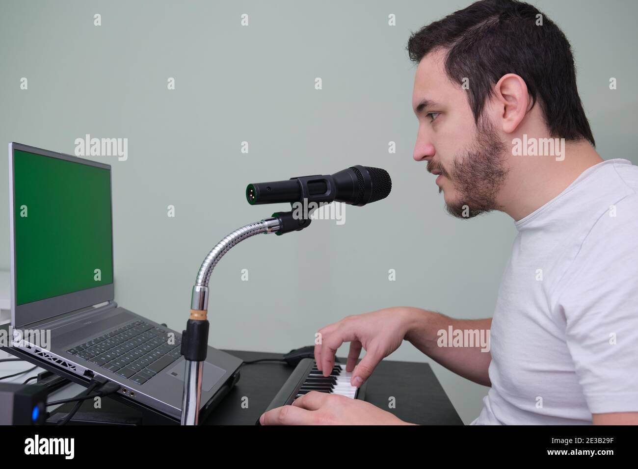 Un homme apprenant à jouer du piano électronique sur Internet à la maison. Écran vert sur l'ordinateur portable. Banque D'Images