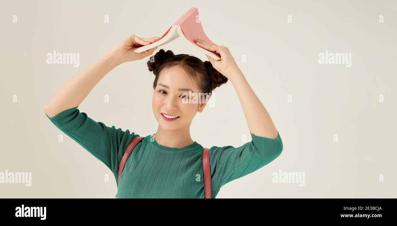 Portrait isolé de la jeune femme souriante en t-shirt vert debout avec le livre sur sa tête Banque D'Images