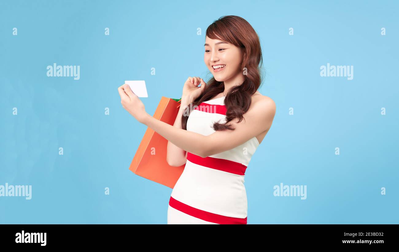 Tendance belle jeune femme asiatique portant des sacs colorés shopping en ligne avec téléphone portable isolé sur fond bleu Banque D'Images