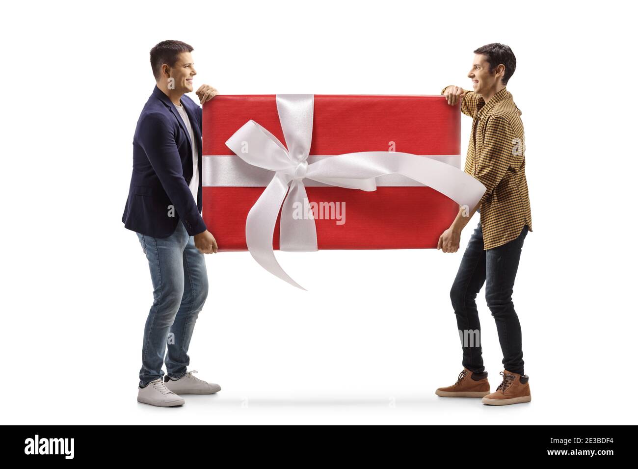 Photo de profil pleine longueur de deux jeunes hommes portant un grand cadeau enveloppé isolé sur fond blanc Banque D'Images