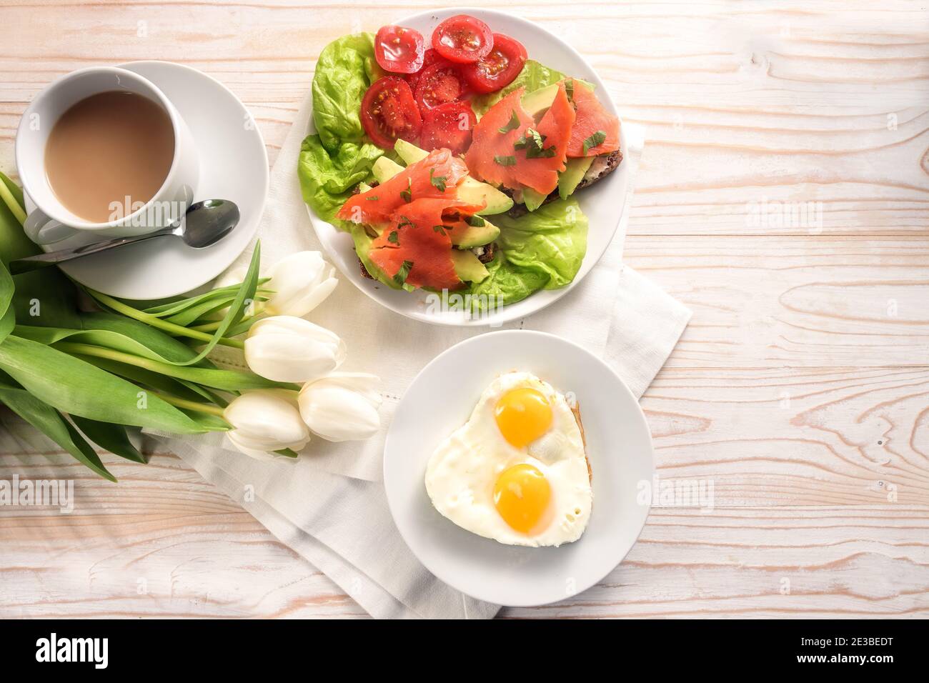 Petit déjeuner sain préparé avec amour, œufs frits en forme de coeur, sandwich avec avocat et saumon fumé sur salade de laitue et de tomate, café et blanc Banque D'Images