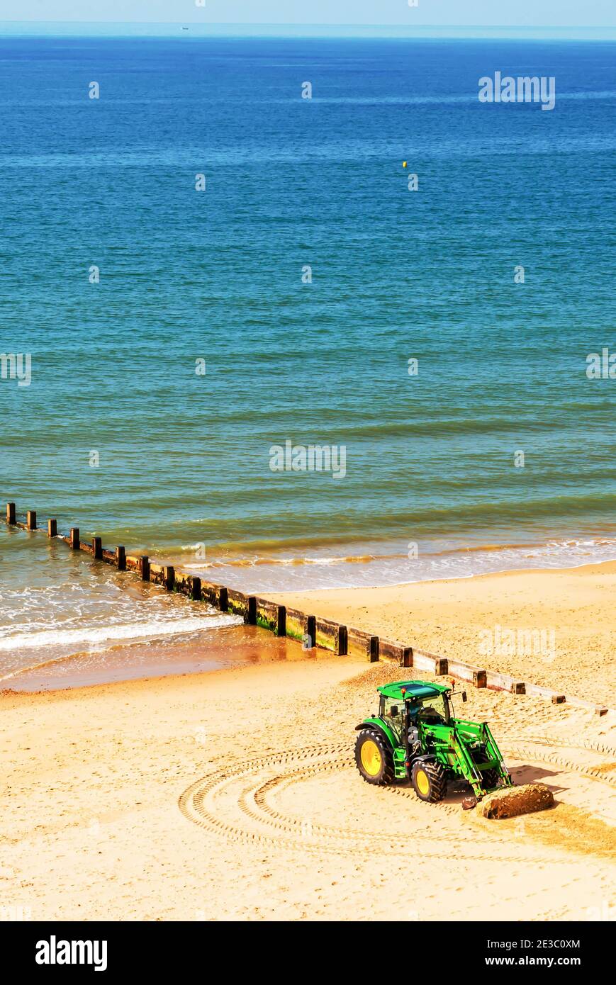 Un tracteur déplaçant du sable sur une plage anglaise par une journée ensoleillée en arrière-plan magnifique océan, industrie côtière Banque D'Images