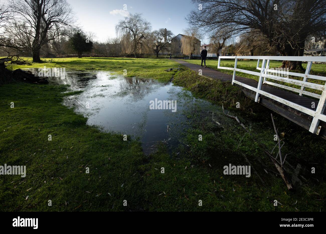 Personne seule marchant à travers Sheeps Green sur le chemin avec blanc Pont avec ruisseau inondé à Cambridge en Angleterre Banque D'Images