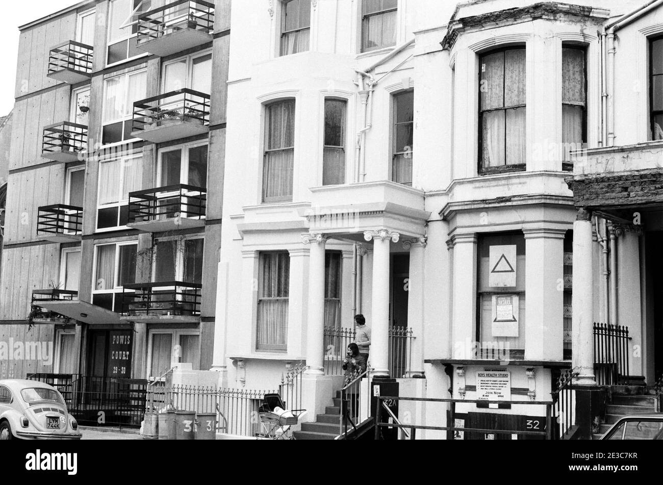 Royaume-Uni, West London, Notting Hill, 1973. Les grandes maisons de quatre étages en ruine et en ruine commencent à être restaurées et redécorées. Appartements modernes à Powis court à gauche. No.32 Powis Square - panneau 'Roys Health Studio'. Affiche dans la fenêtre pour un bazar d'étoile de mornig. Banque D'Images