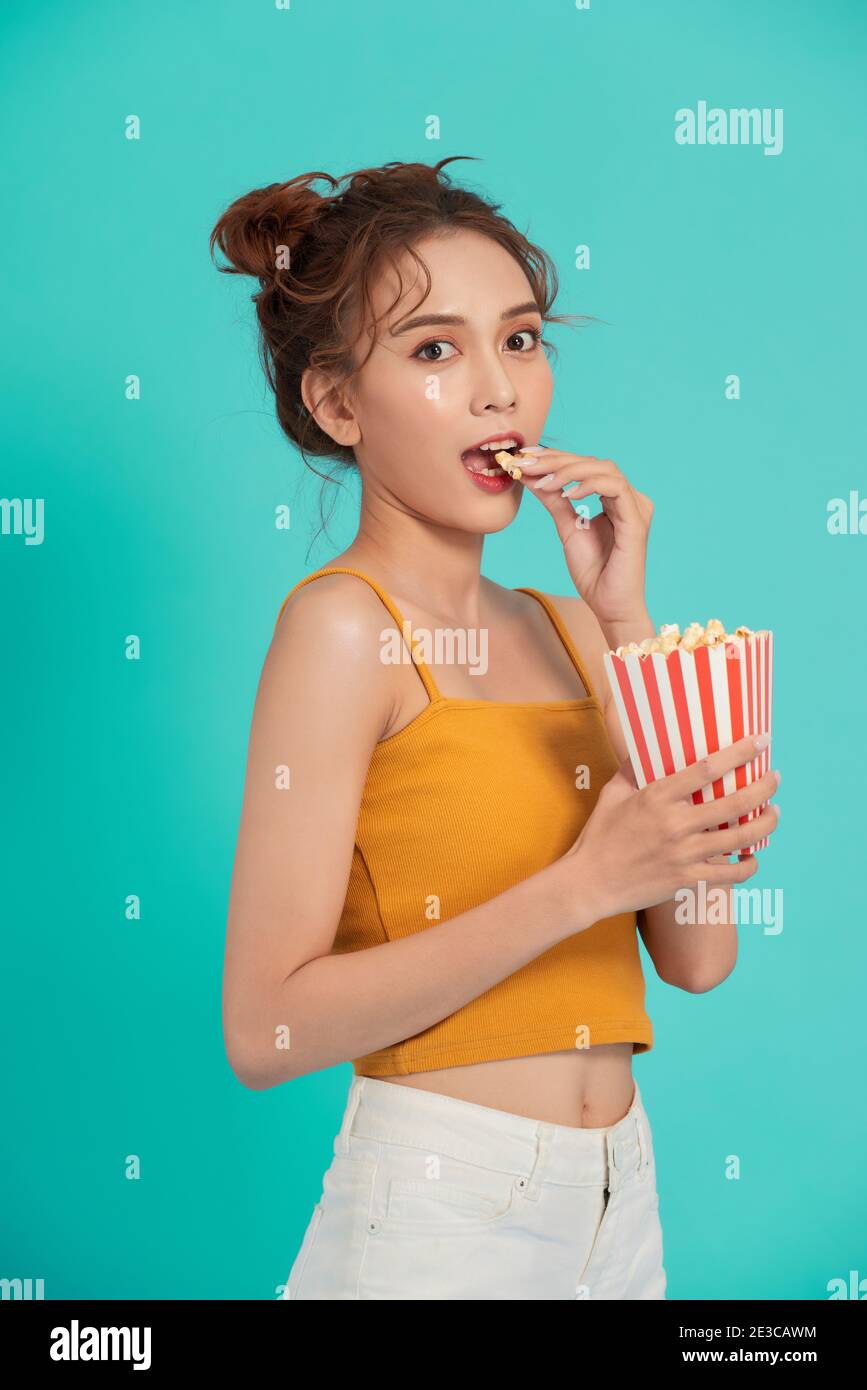 Portrait d'une fille qui rit dans des vêtements décontractés tenant du pop-corn et en regardant la caméra isolée sur un arrière-plan lumineux Banque D'Images