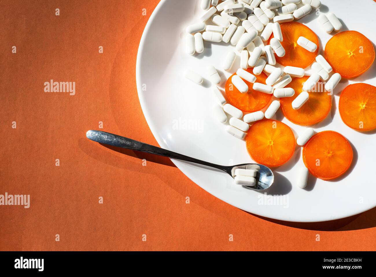 Sur une assiette ovale blanche - tranches d'orange de persimmon, capsules de suppléments minéraux et une cuillère avec une pilule. Orange. Biohaking sur des sujets de santé. Banque D'Images