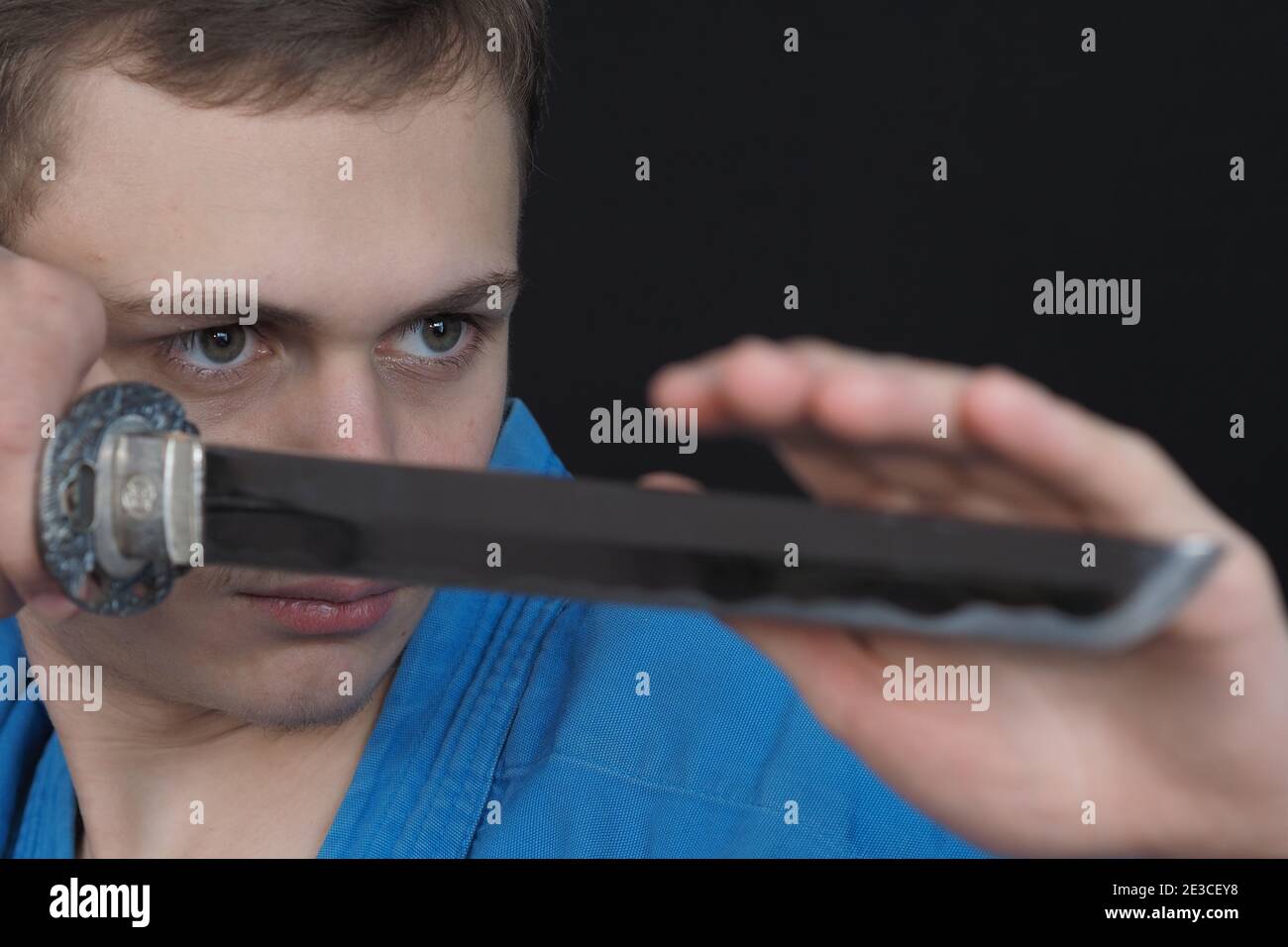 Portrait d'un jeune homme dans un kimono bleu avec une épée. Arrière-plan noir. Banque D'Images