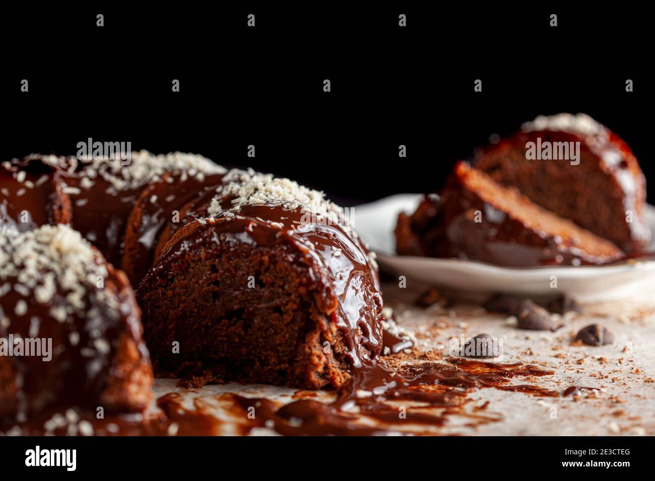 Vue latérale inclinée d'un gâteau au chocolat rond gastronomique avec des noix de coco râlées sur la glace. Deux tranches ont été retirées et placées sur une plaque en porcelaine blanche avec un moi Banque D'Images