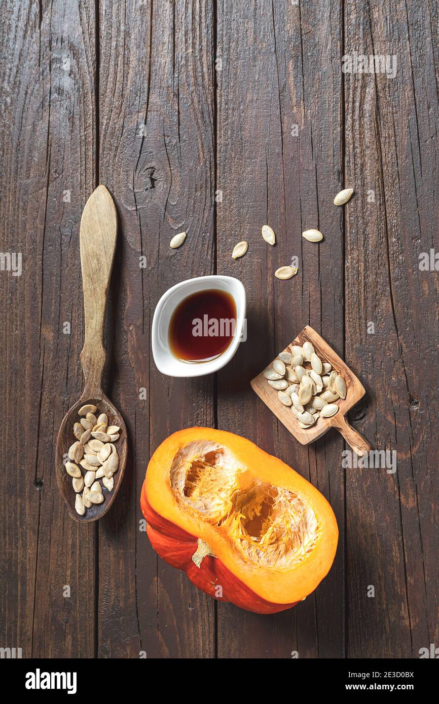 Un bol blanc avec de l'huile de graines de citrouille, des graines de pumkin en cuillères en bois et de la pumkin d'automne frais sur une vieille table en bois sombre, vue verticale du dessus avec Copy spa Banque D'Images