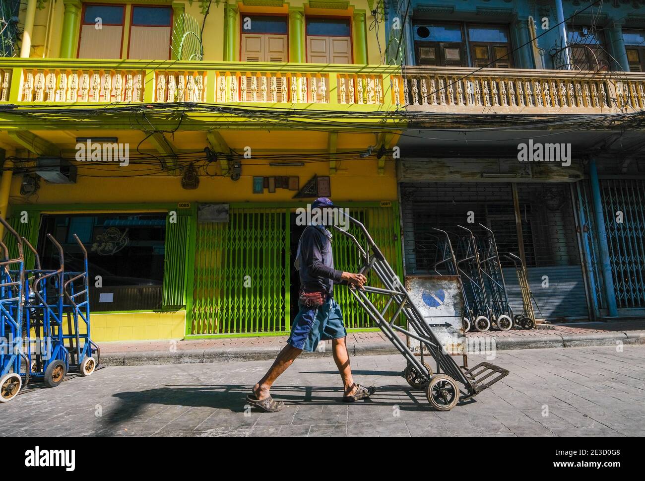Un homme pousse un chariot vide le long d'une route ensoleillée à Chinatown, Bangkok, Thaïlande Banque D'Images