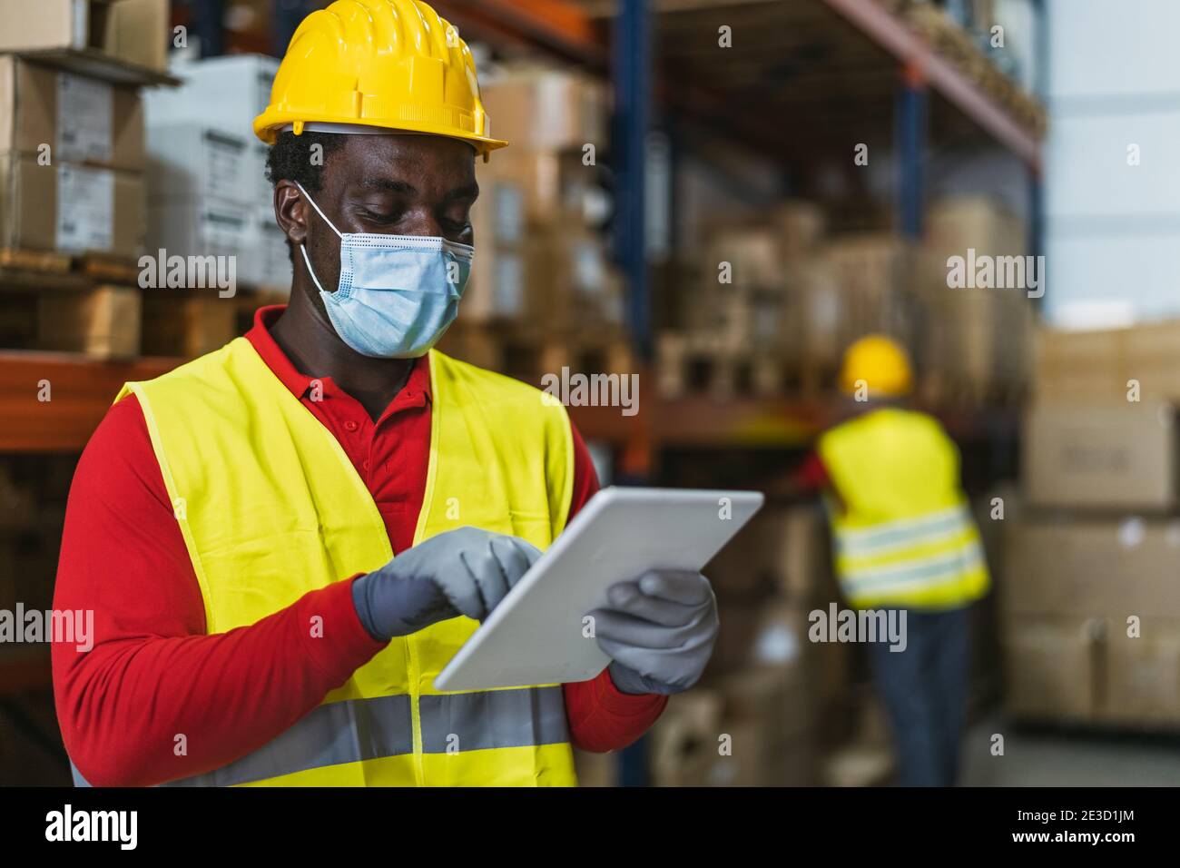 Homme noir travaillant dans un entrepôt effectuant un inventaire à l'aide d'une tablette numérique et le chargement des boîtes de livraison sont prévu pendant le port du masque facial virus corona Banque D'Images