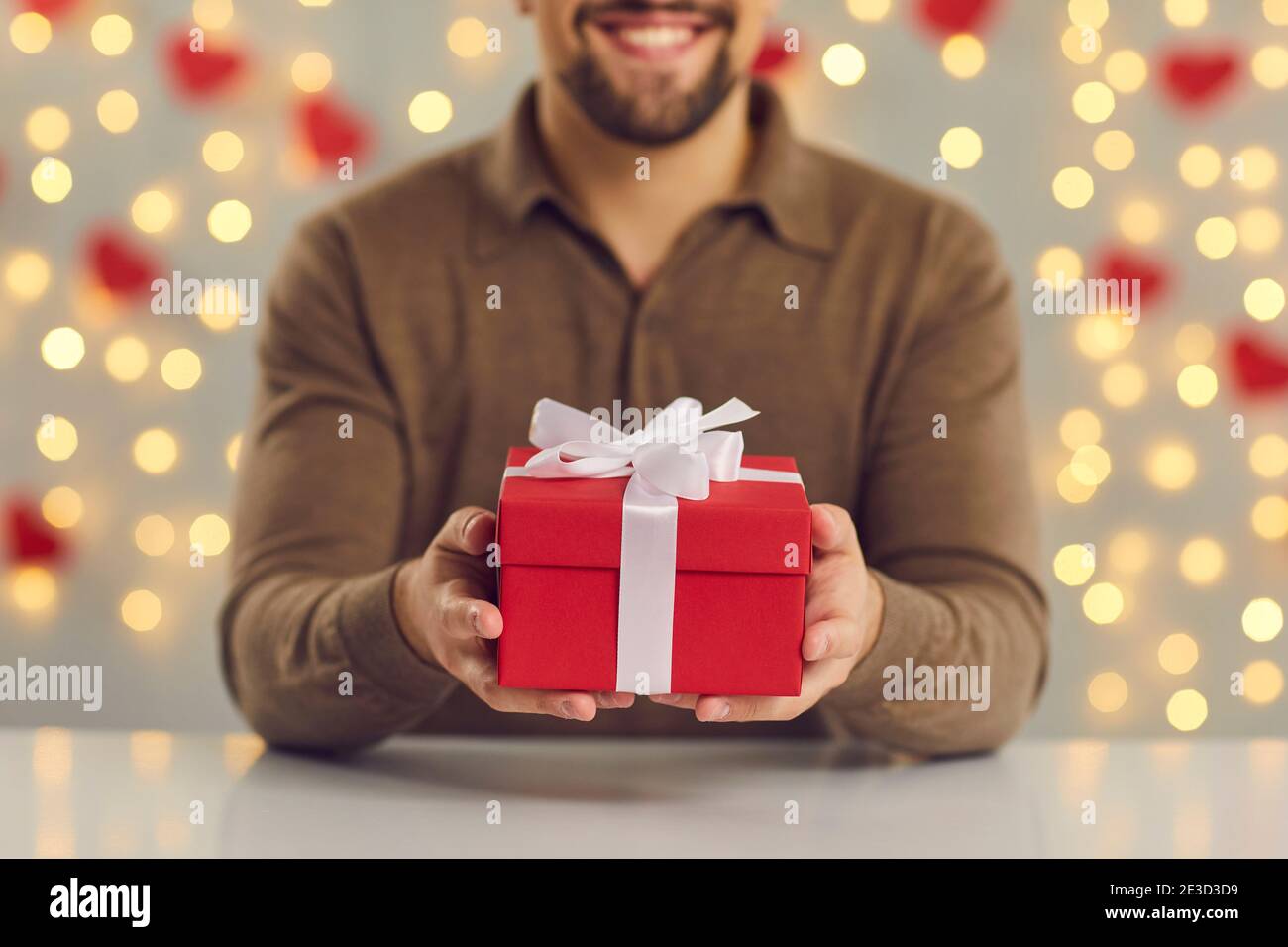 Image rognée en gros plan d'une boîte cadeau rouge avec un noeud blanc dans les mains des hommes assis à la table. Banque D'Images
