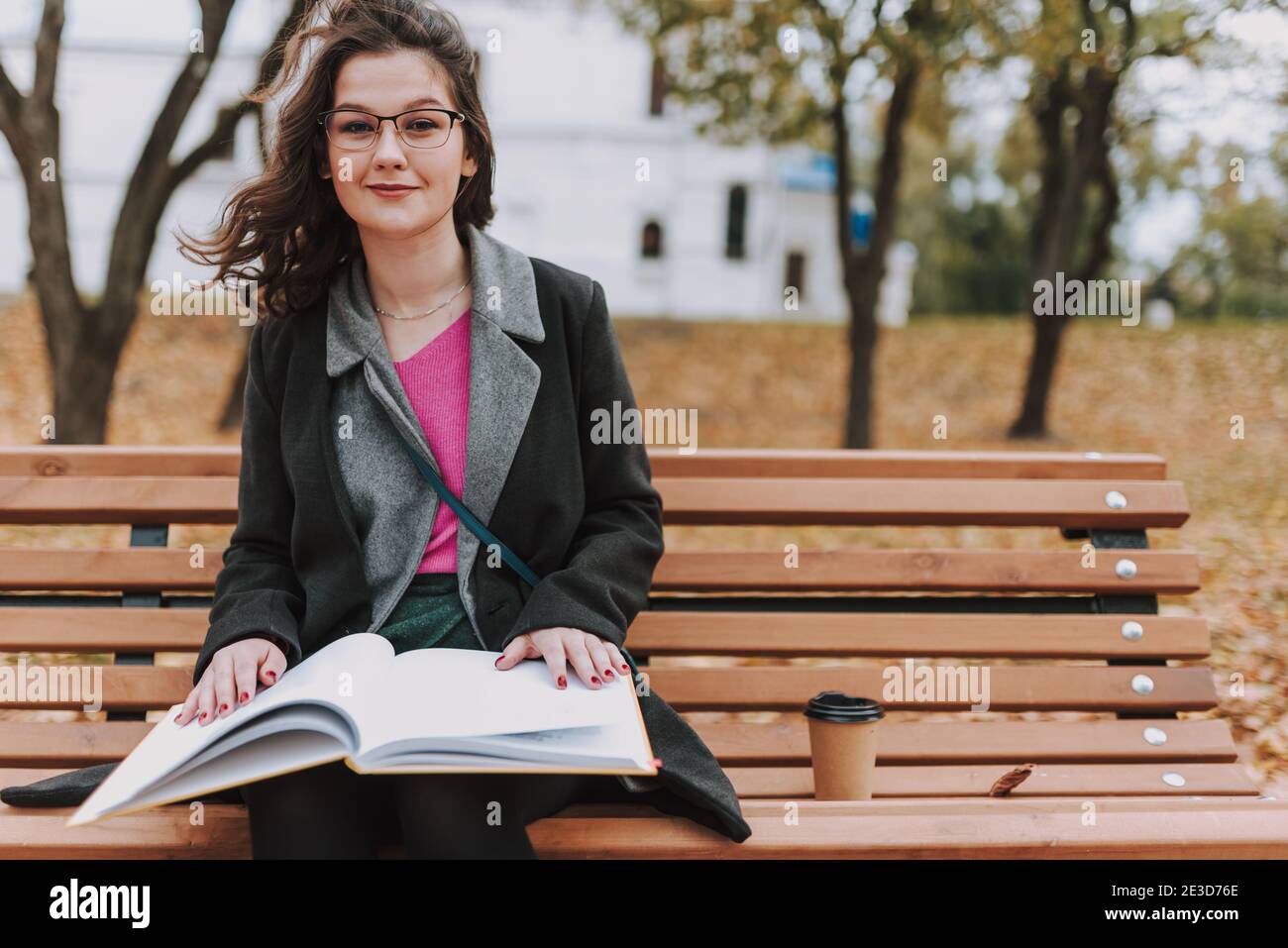 Femme étudiante souriante assise sur le banc avec une boisson chaude et réservez à l'extérieur Banque D'Images