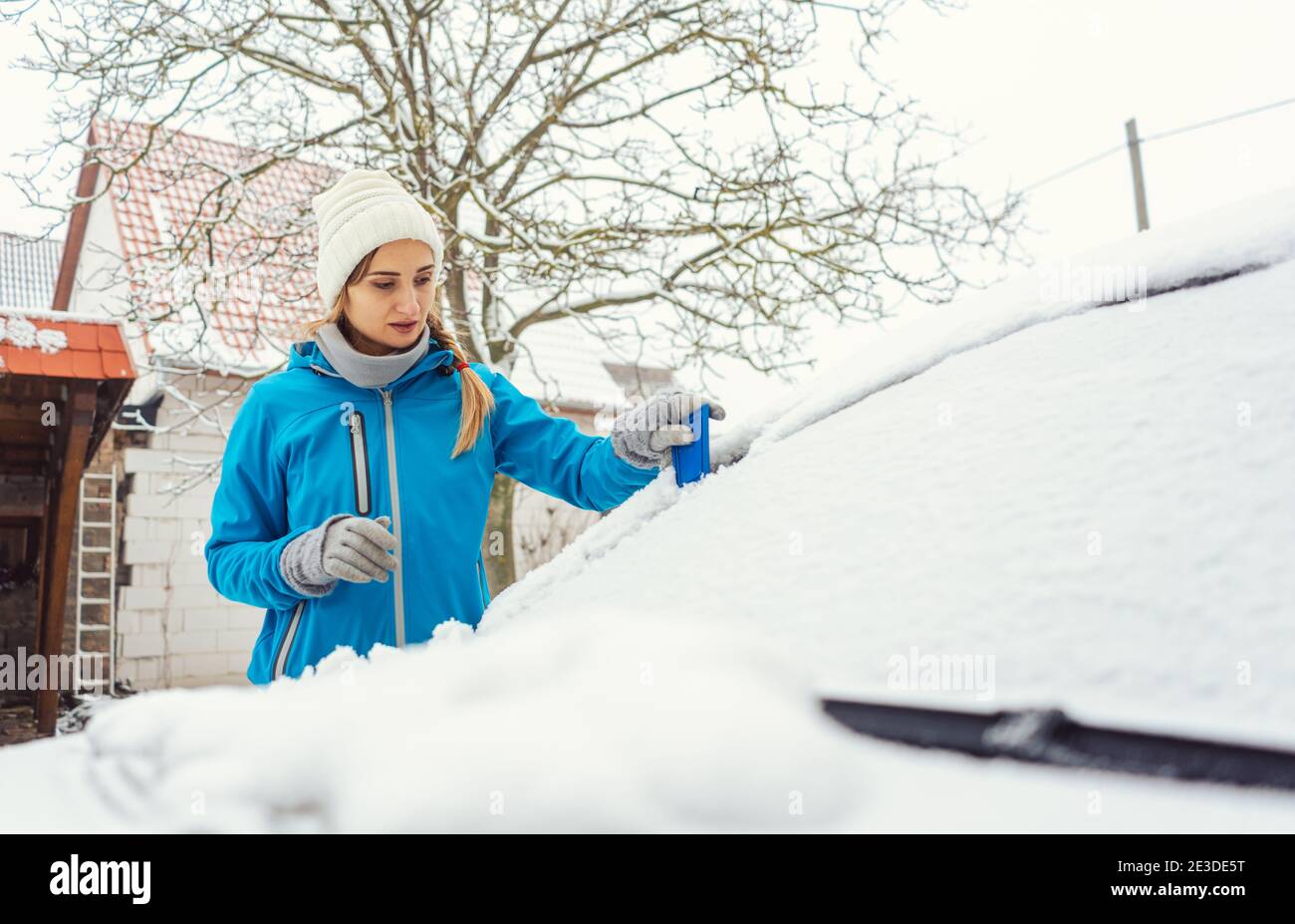 Femme raclant la glace de la fenêtre avant de sa voiture en hiver Banque D'Images