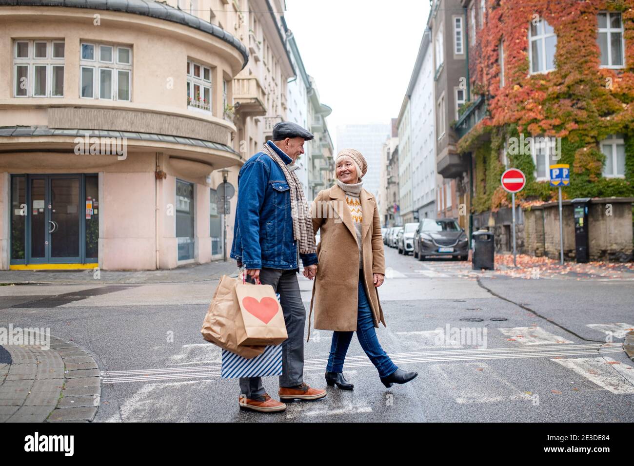 Heureux couple senior marchant à l'extérieur dans la rue dans la ville, portant des sacs de shopping. Banque D'Images