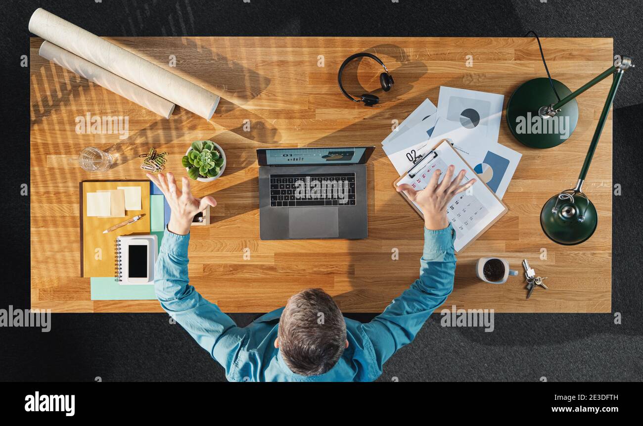 Vue de dessus d'un homme d'affaires en colère travaillant sur un ordinateur au bureau avec des documents dans le bureau à la maison. Banque D'Images