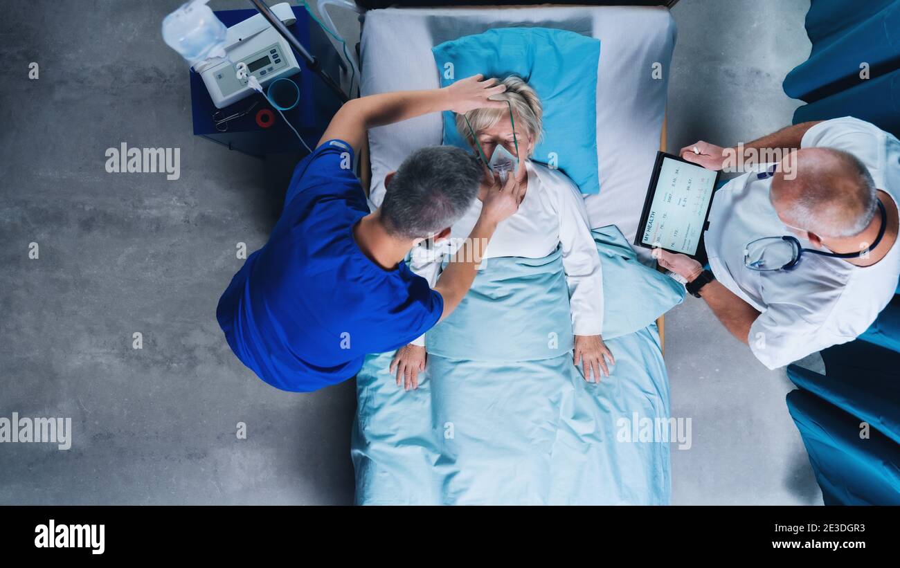 Vue de dessus des médecins et patient Covid-19 avec masque d'oxygène dans le lit à l'hôpital, concept de coronavirus. Banque D'Images