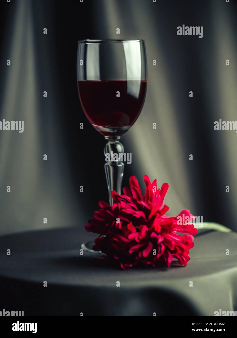 Sur la table se trouve un verre de vin rouge. À proximité est une fleur rouge. Flou artistique. Banque D'Images