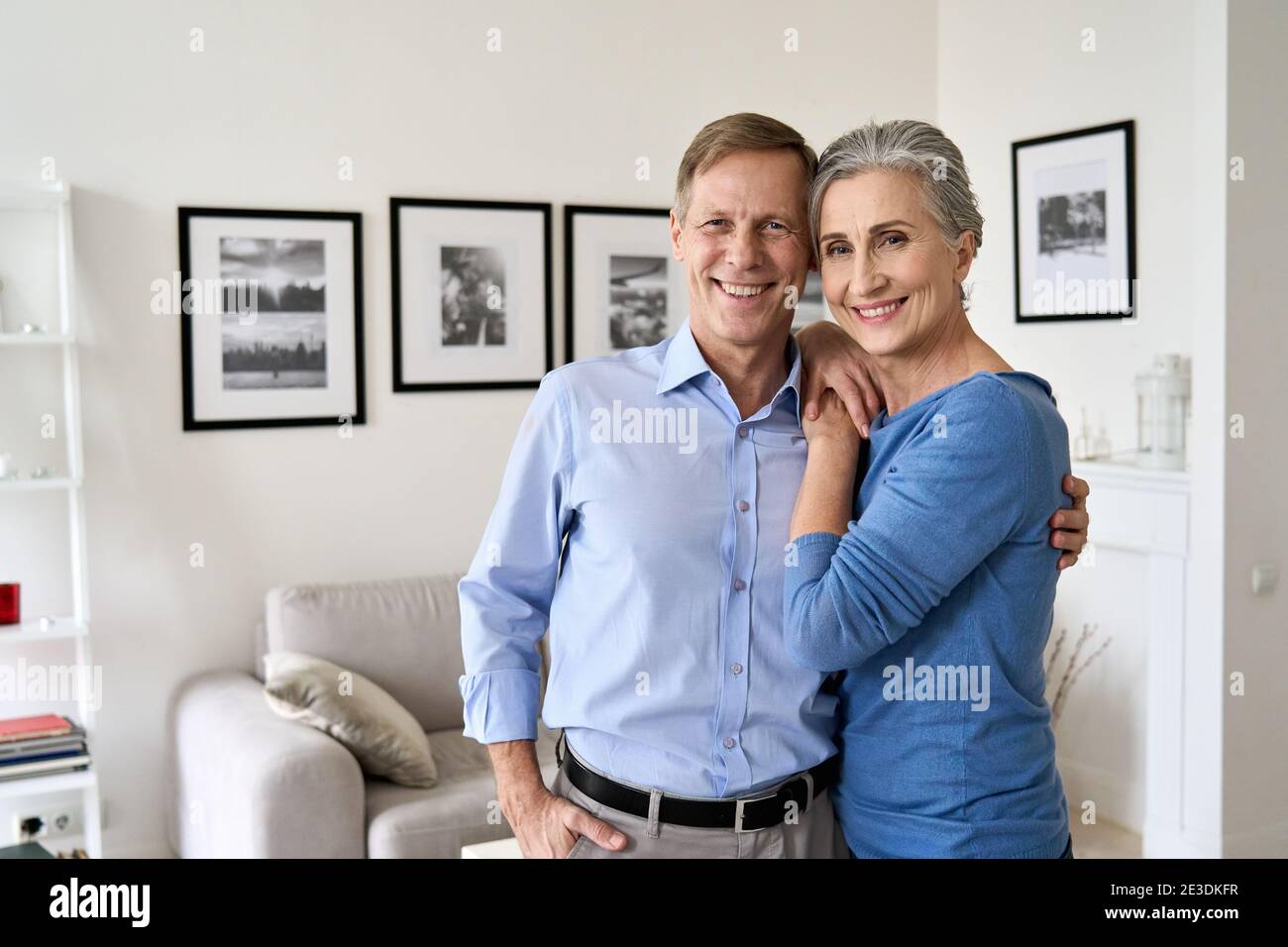 Heureux couple plus âgé qui se hoit, regardant la caméra, assis sur un canapé dans l'appartement. Banque D'Images
