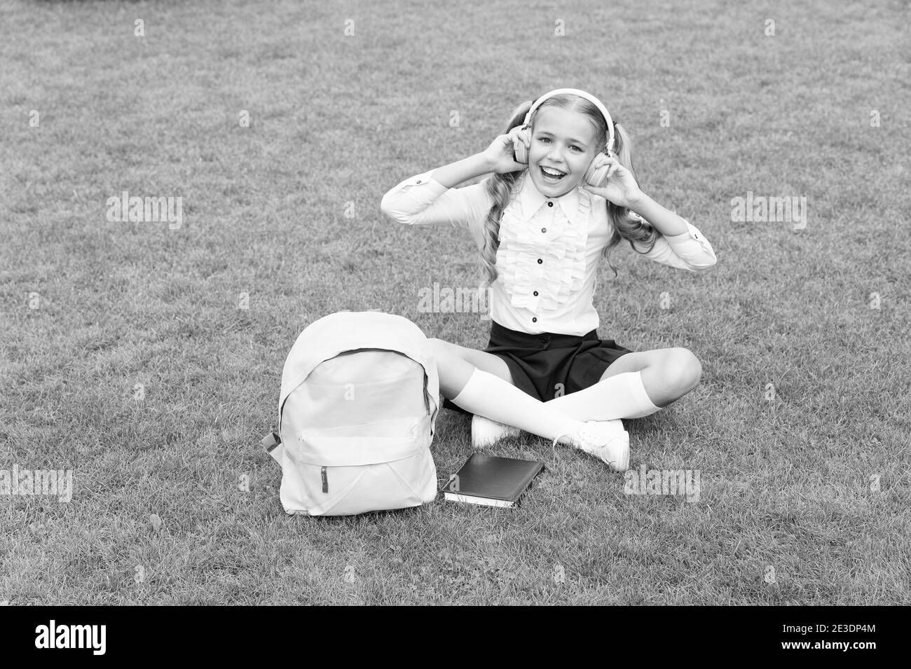 L'éducation est un meilleur ami. Concept d'éducation. Journée ordinaire d'apprentissage en ligne. Fille écouter de la musique. Fille d'école maternelle heureuse avec livre dans la cour d'école. Retour à l'école. Enfant dur porter des écouteurs. Banque D'Images