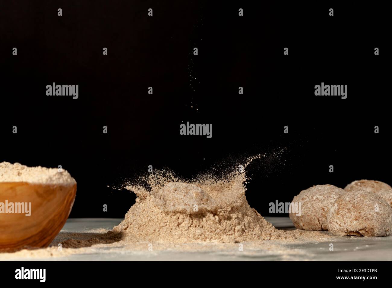 Fabrication de pain maison avec un bol en bois de farine et quelques creux sur le fond. Une autre pâte est en train de tomber dans une pile de farine sur le comptoir en marbre Banque D'Images