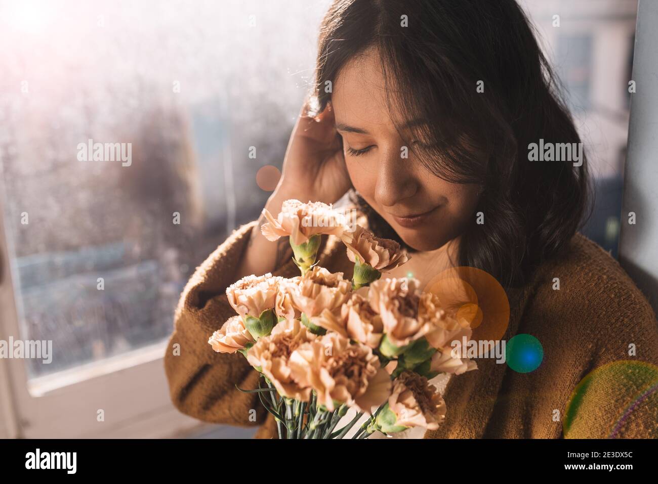 belle jeune femme sentant un bouquet de fleurs de gillyflowers roses à la maison par fenêtre. yeux fermés, expression détendue authentique et aspect naturel. pas de maquillage Banque D'Images