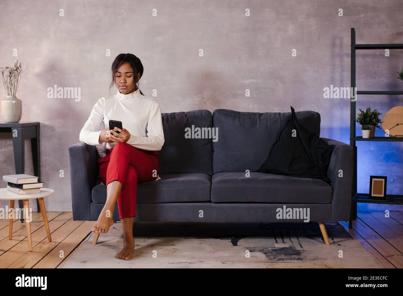 Une fille africaine regarde son téléphone sur le canapé sa chambre confortable Banque D'Images