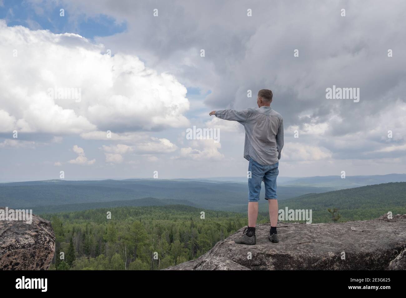 Un homme d'âge moyen se dresse au sommet de la montagne et montre où aller. Concept de voyage et de vie active. Réalisation de l'objectif. Copier l'espace Banque D'Images