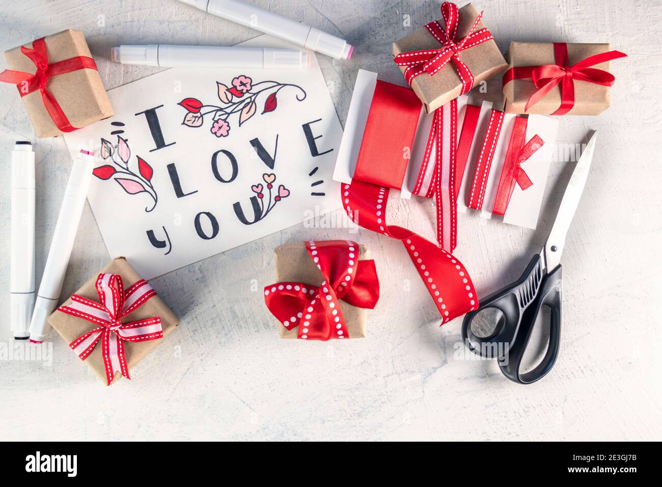 Rubans rouges, cadeaux, ciseaux, marqueurs à côté de la Valentin avec les mots Je t'aime. Préparation pour la Saint-Valentin. Concept de la Saint-Valentin. Pose à plat. Vue de dessus Banque D'Images