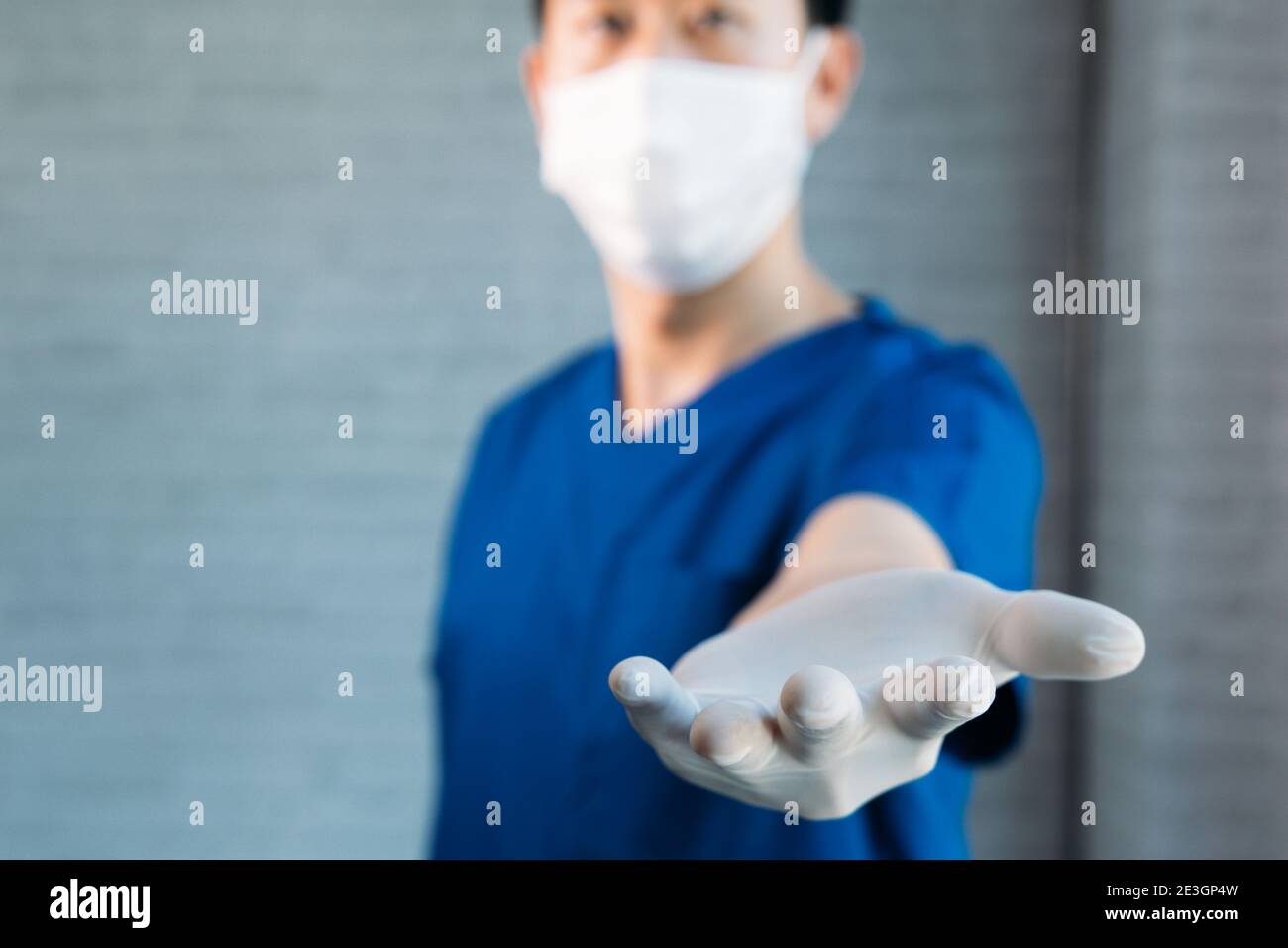 Travailleur médical masculin dans les exfoliants portant des gants et un masque chirurgical, donnant les mains pour offrir un soutien avec l'espace de copie Banque D'Images