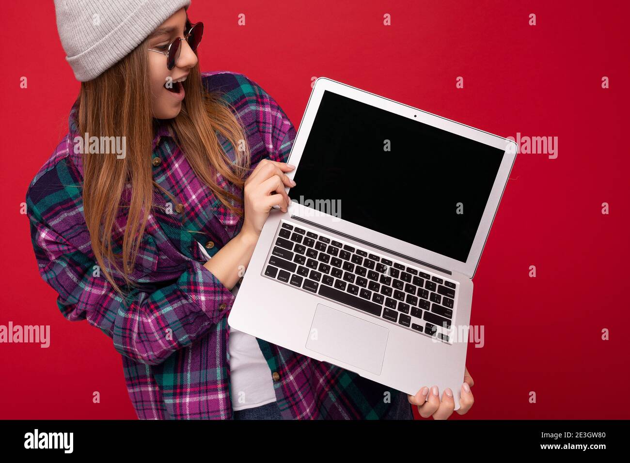 Portrait photo de beau rire drôle souriant blonde jeune femme tenir un ordinateur portable avec un écran de moniteur vide et porter des lunettes de soleil chapeau et Banque D'Images