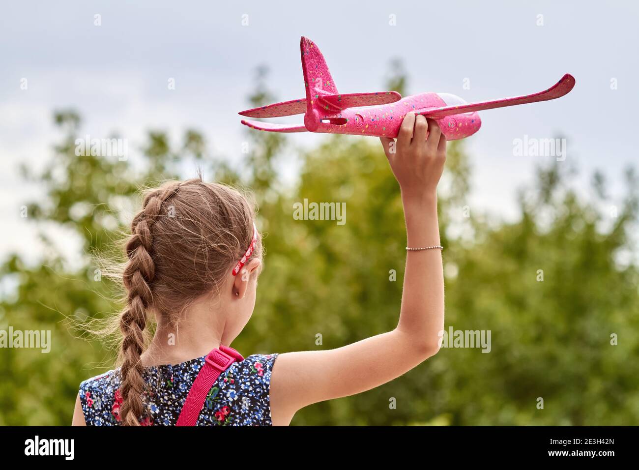 Fille lançant un avion de jouet rose dans l'air contre le fond des arbres et du ciel. Banque D'Images