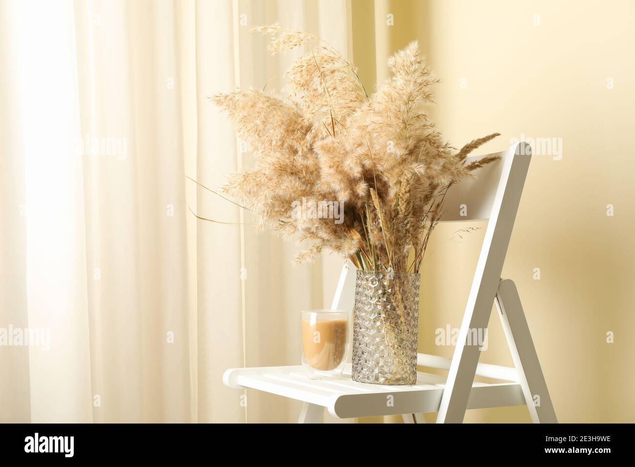 Chaise rustique avec un bouquet de fleurs sauvages des champs dans un vase et un verre à latte, un moment latte estival avec des fleurs des champs pour une ambiance café cosy Banque D'Images