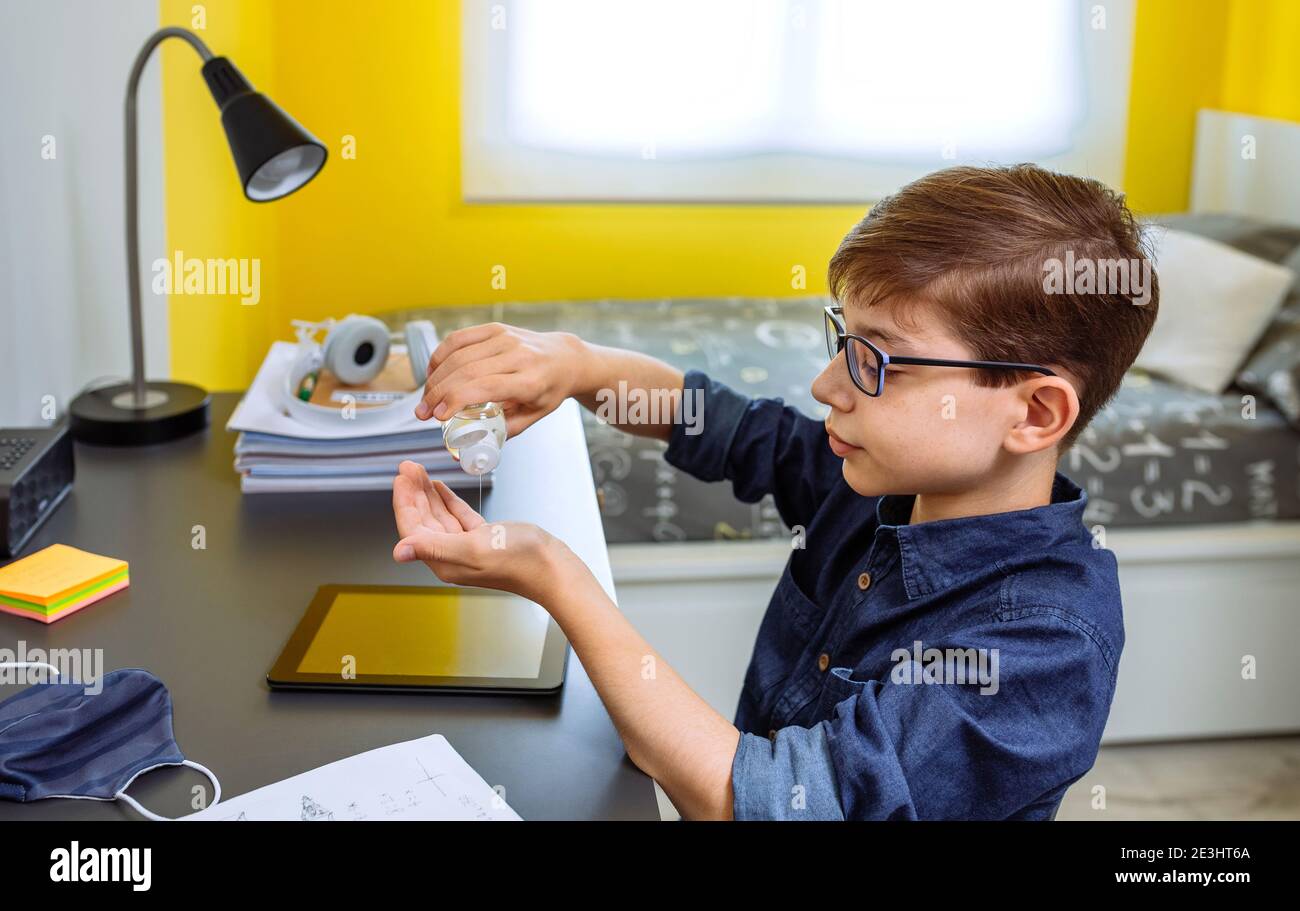 Adolescent appliquant de l'assainisseur pour les mains avant de faire ses devoirs Banque D'Images