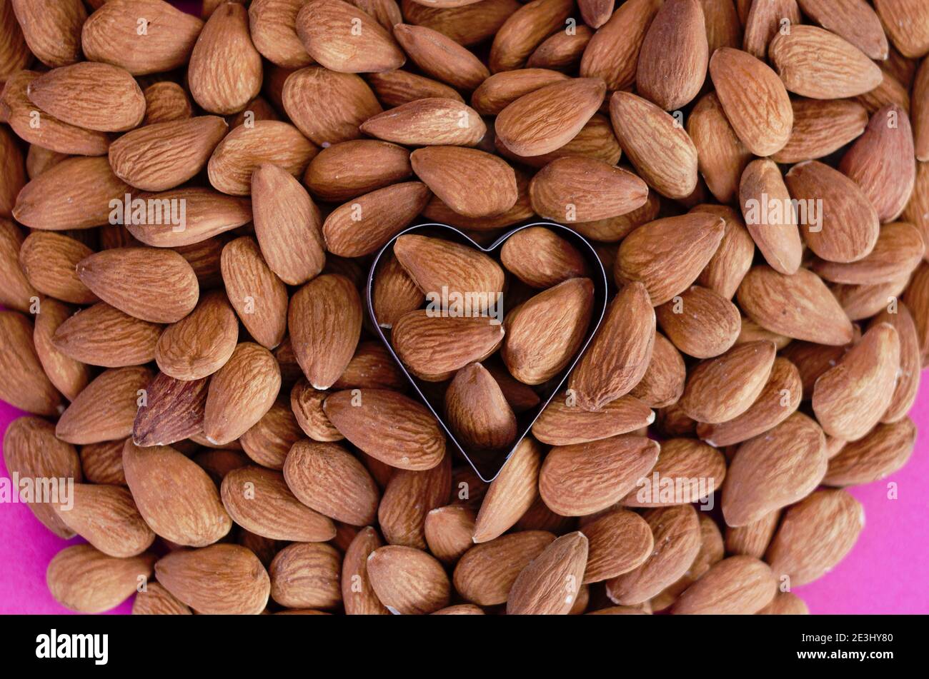 Tas d'amandes en forme de coeur sur fond rose. Isolé. Saint Valentin. Pose à plat. Vue de dessus. Aliments crus. Banque D'Images