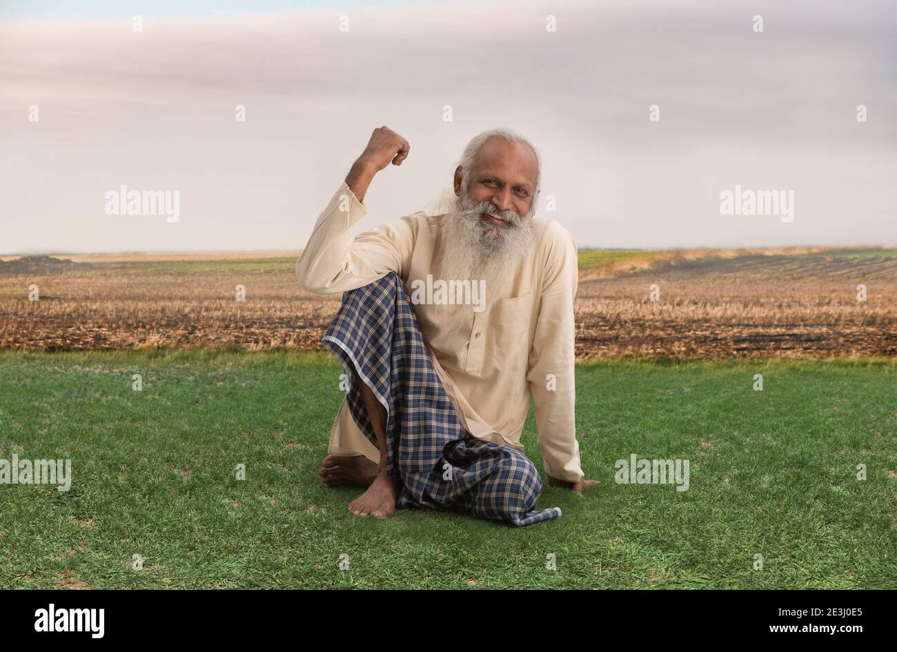 UN VIEUX FERMIER CONFIANT ASSIS ET SOURIANT À LA CAMÉRA Banque D'Images