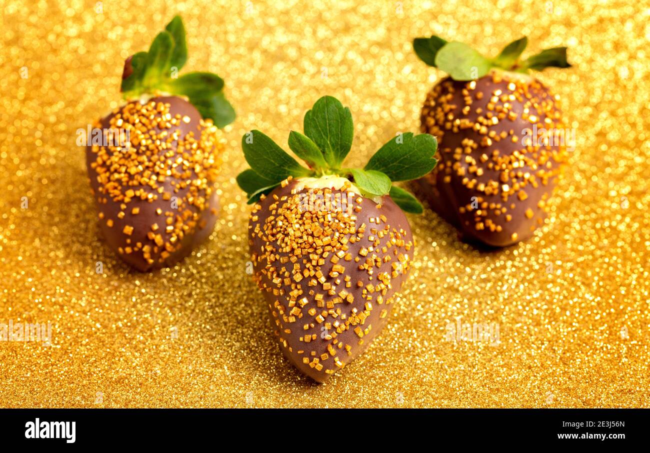 Fraises enrobées de chocolat recouvertes de Sprinkles sur une Glitterie dorée Arrière-plan Banque D'Images