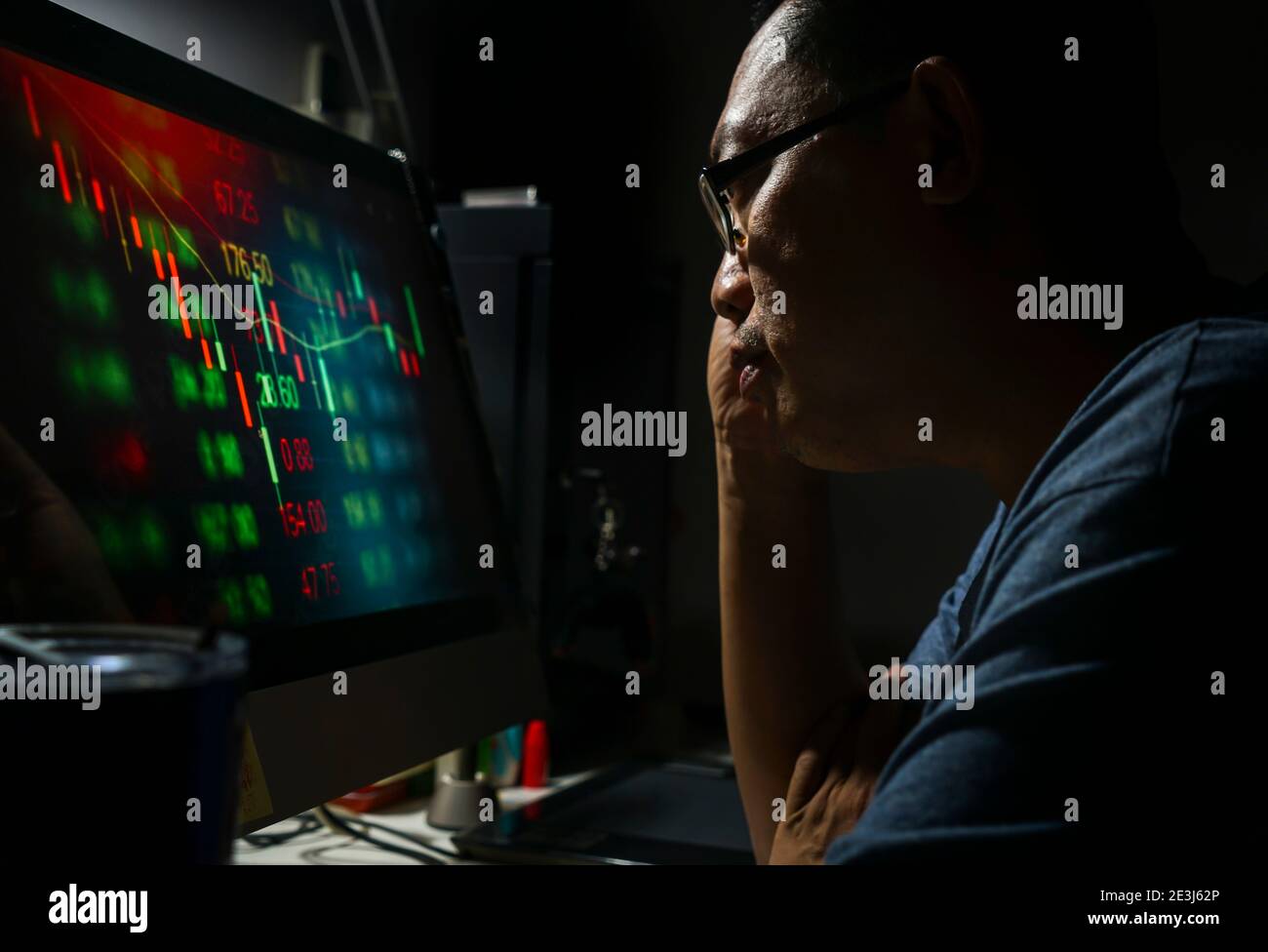 Gros plan asiatique d'âge moyen homme analysant le graphique de chandelier de commerce d'investissement de marché boursier sérieusement à partir d'ordinateur dans sa chambre la nuit. Banque D'Images