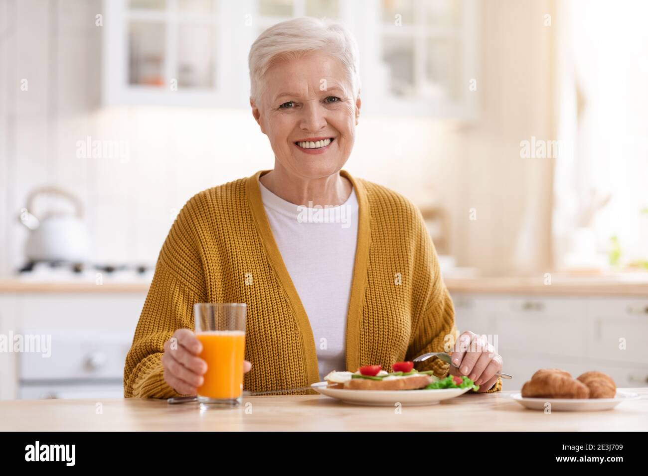 Belle grand-mère souriant à l'appareil photo, déjeuner dans la cuisine Banque D'Images
