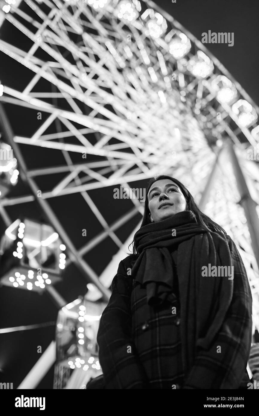 Jeune belle femme brune caucasienne posant par la roue de ferris la nuit. Photos en noir et blanc Banque D'Images