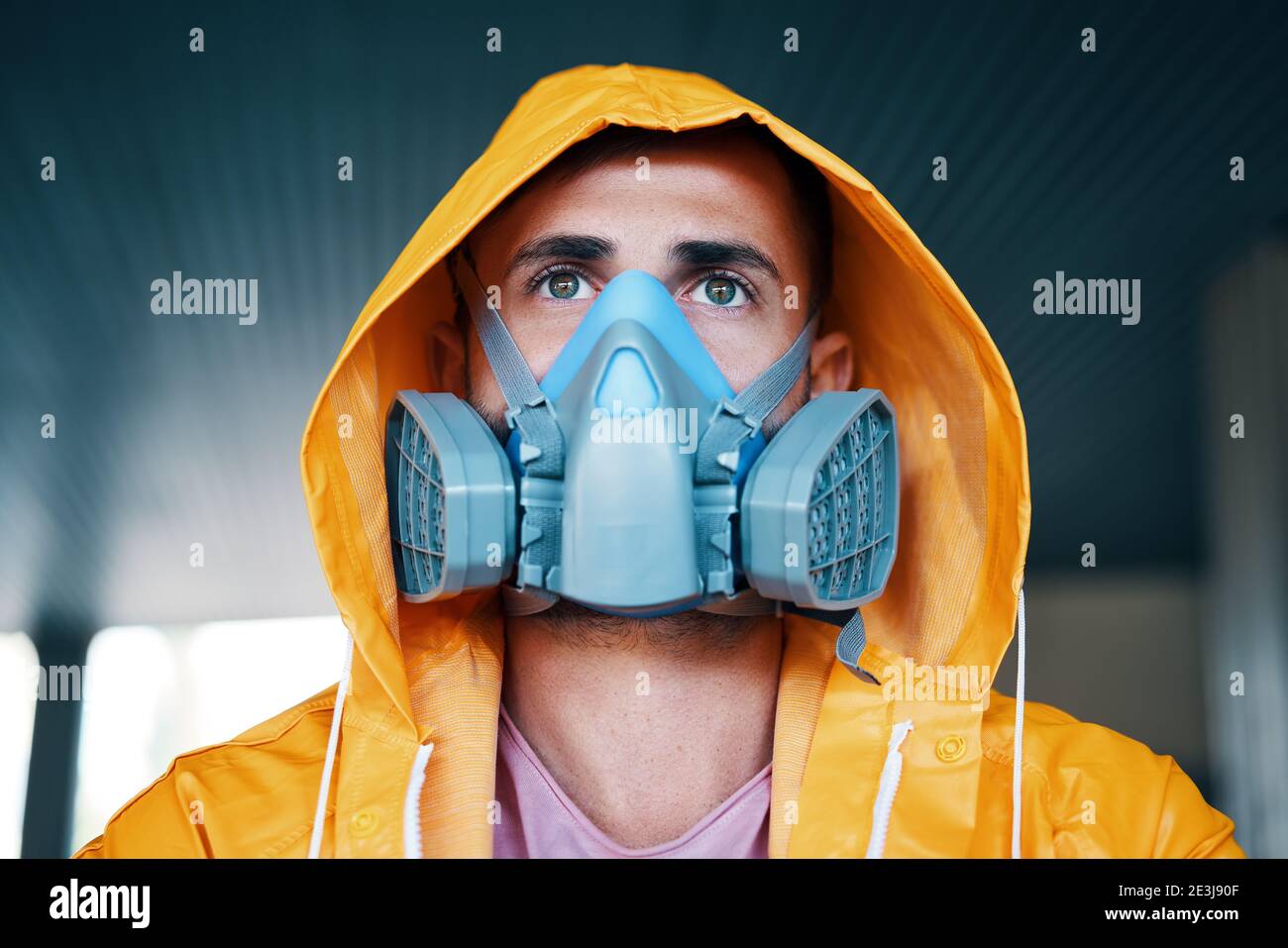 Gros plan du jeune homme dans un masque respiratoire et imperméable jaune posé dans la rue et regardant la caméra Banque D'Images