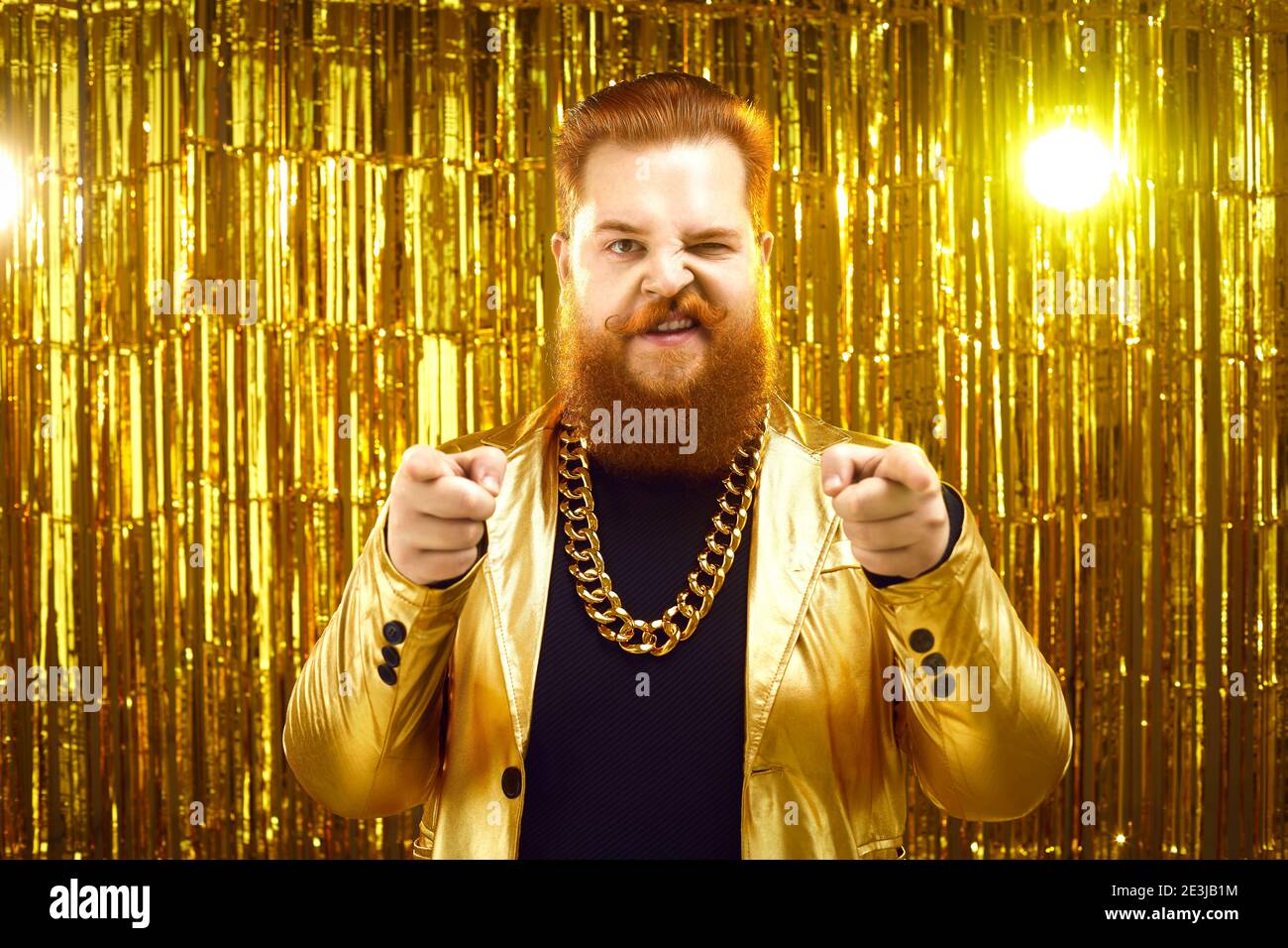 Homme extravagant en blouson doré funky, avec chaîne d'or autour du cou, pointant vers l'appareil photo Banque D'Images