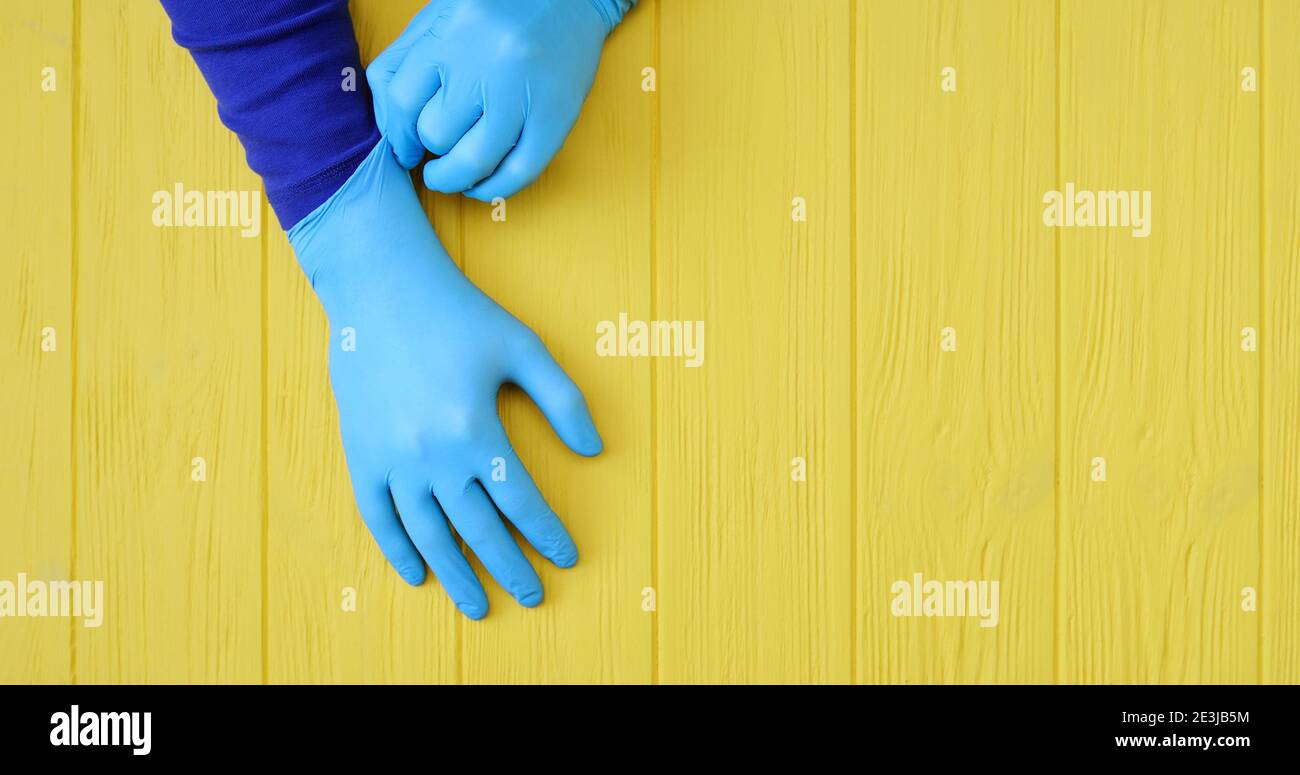 Gants en nitrile bleu bannière. Mains d'un médic dans les gants en latex bleu sur un fond en bois jaune avec place pour votre texte Banque D'Images