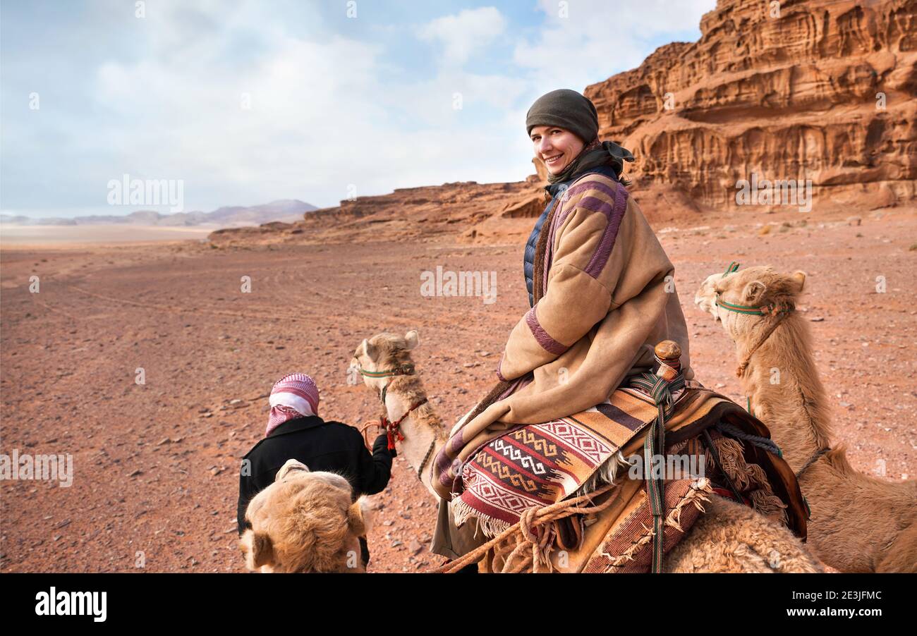 Jeune femme à cheval à dos de chameau dans le désert de Wadi Rum, en  regardant derrière son épaule, souriant. Il fait très froid, elle porte  donc un manteau bédouin traditionnel -