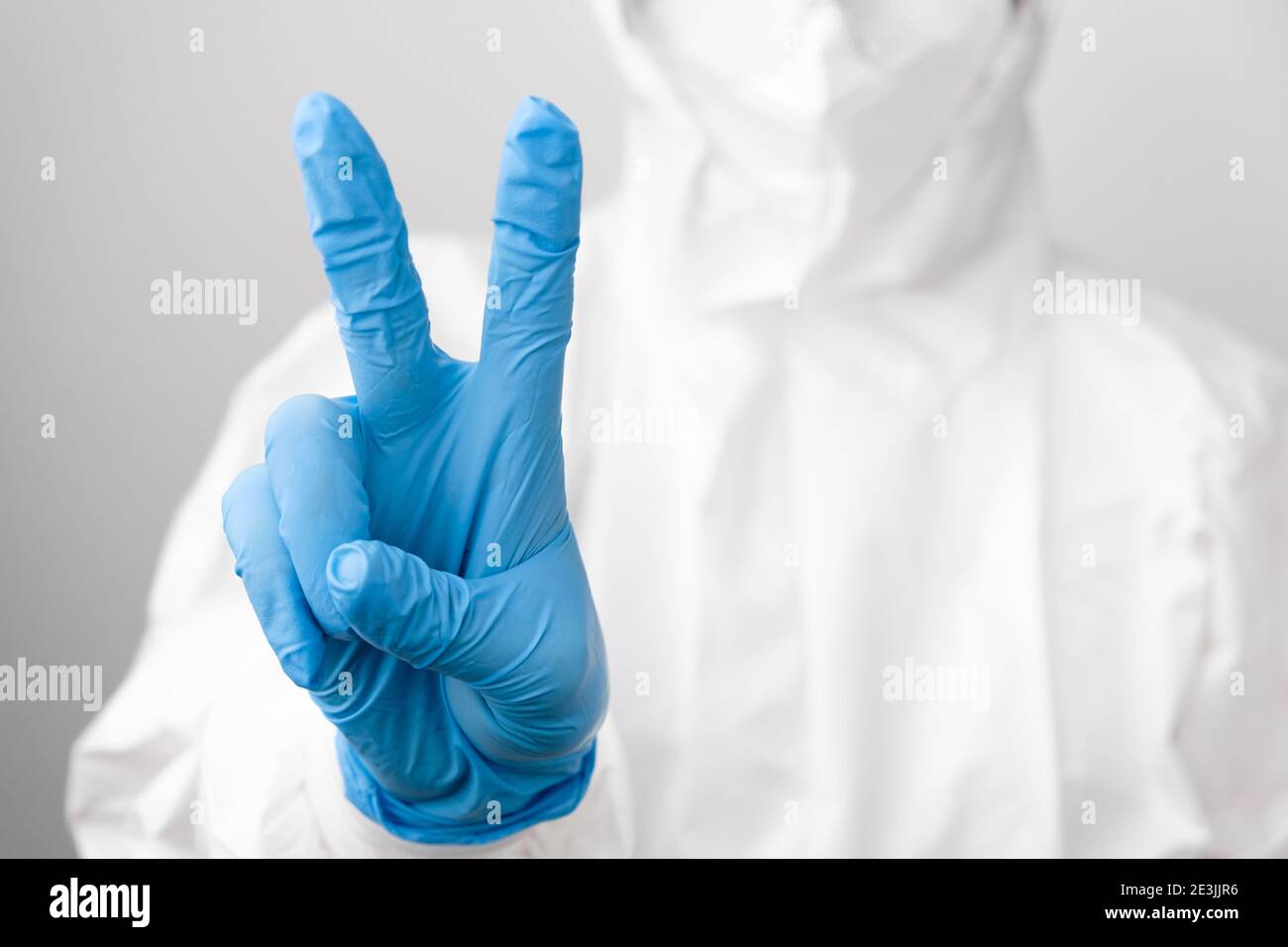 Médecin dans un vêtement de protection en PPE et un masque facial de protection contre le coronavirus, SARS-COV-2, Covid-19 montre signe de paix dans les gants en caoutchouc bleu. Banque D'Images