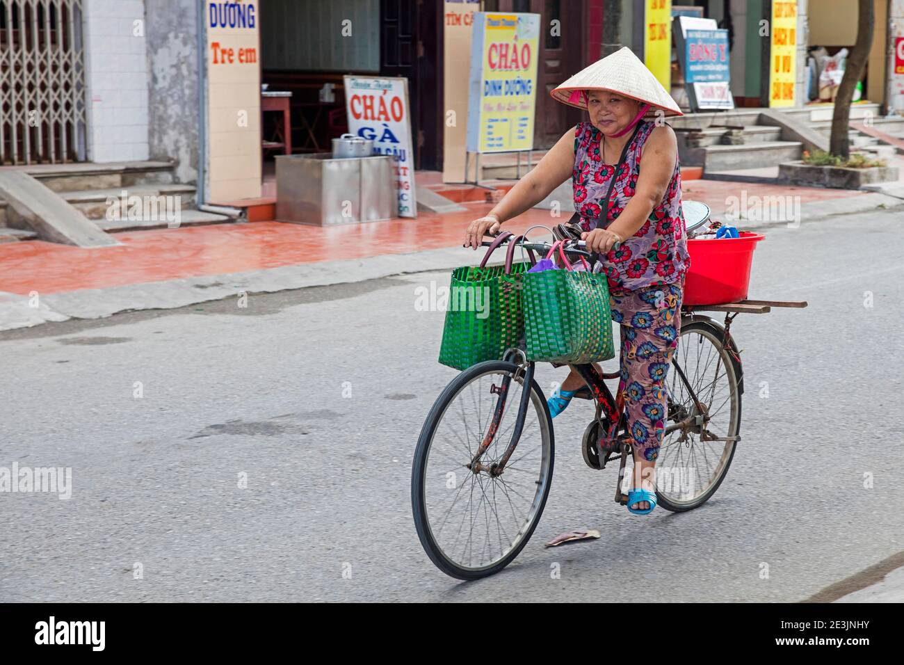 Femme vietnamienne à vélo, portant le traditionnel nón lá, chapeau conique asiatique, dans la ville de Ninh Binh dans le delta de la rivière Rouge du nord du Vietnam Banque D'Images