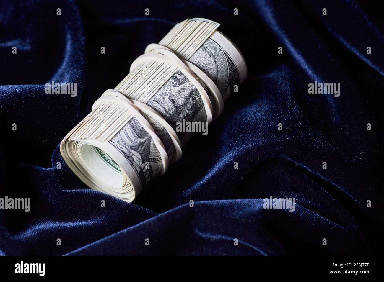 Un rouleau de 100 billets de banque en dollars américains sur du textile de velours bleu, un fond sombre et moody, un gros plan, un espace de copie, un concept de finance et d'économie de capital Banque D'Images