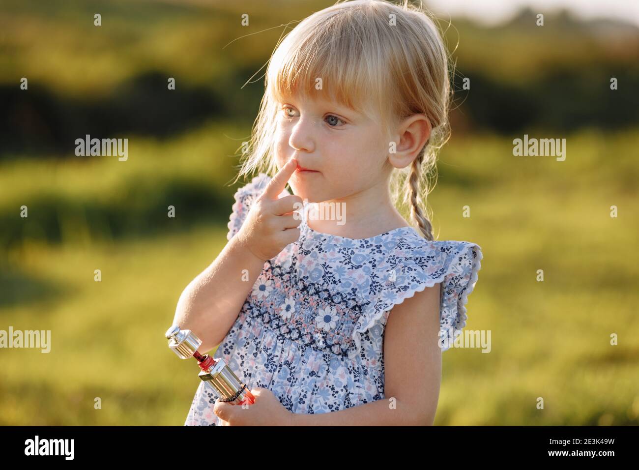 Adorable petite fille rouge ses lèvres avec le rouge à lèvres d'une mère à l'extérieur. Grandir, leadership, copier le concept de comportement de psychologie féminine Banque D'Images