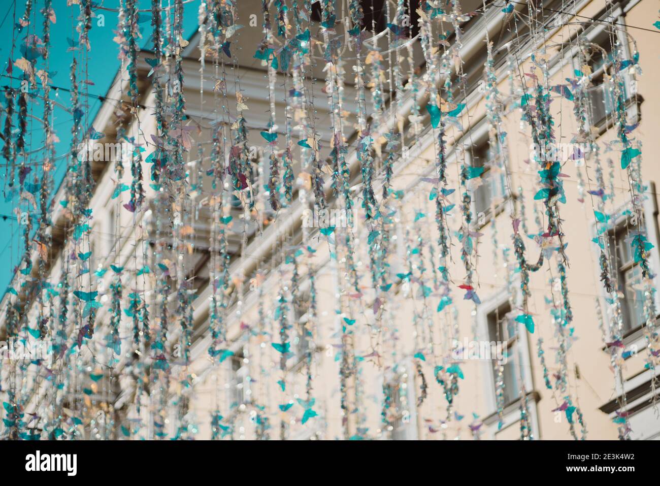 Rue ensoleillée de la ville avec des décorations pendues du haut: Fils avec strung sur eux diverses perles brillantes, guirlandes, papillons en plastique turquoise et t Banque D'Images Rue ensoleillée de la ville avec des décorations pendues du haut: Fils avec strung sur eux diverses perles brillantes, guirlandes, papillons en plastique turquoise et t Banque D'Images