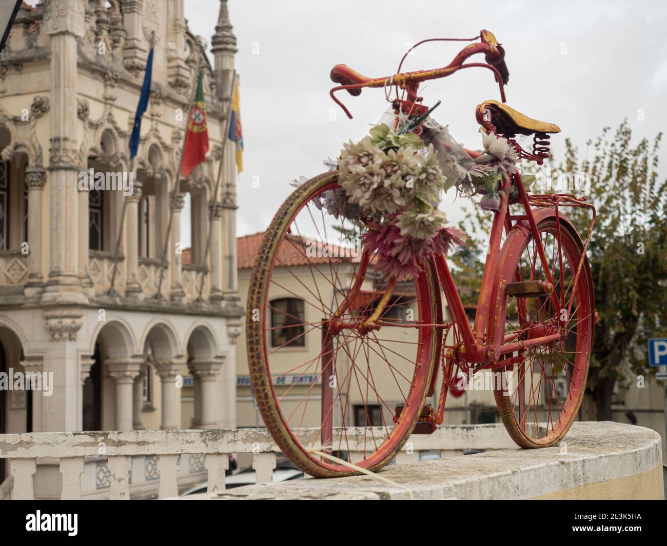 Vieux vélo rouge sur la clôture et un bel hôtel de ville avec les drapeaux de l'Europe, du Portugal et de Sintra en arrière-plan (Câmara Municipal de Sin Banque D'Images